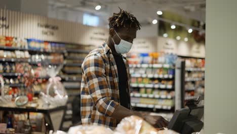 man in mask weighing fruits on the scales in the supermarket