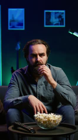 vertical video puzzled man eating popcorn while watching confusing movie on tv