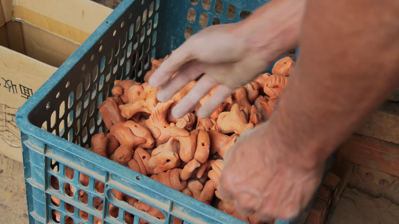 Close up view of hand placing traditional clay figurines in southeast asian pottery style, Than Ha Hoi An Vietnam