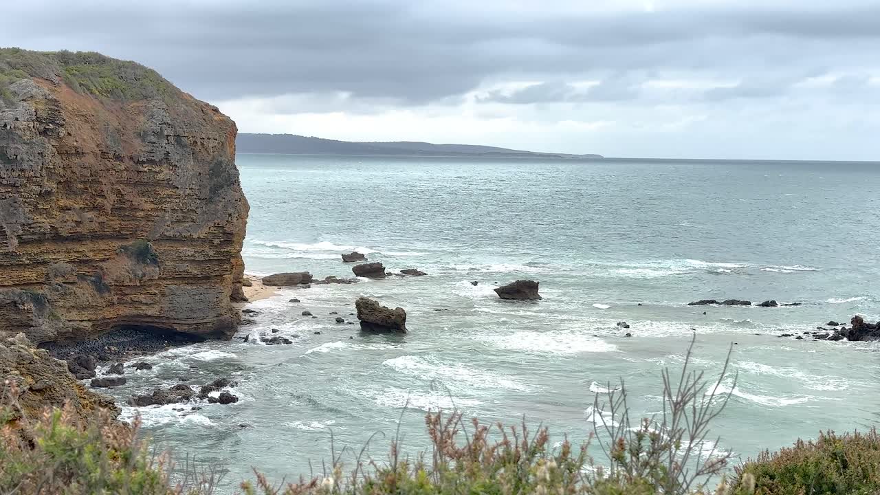 Dramatic coastal cliffs and serene ocean waves under overcast skies at Port Campbell, Australia. Captured with steady camera and natural lighting