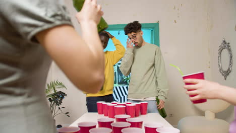 happy multiethnic young friends playing beer pong at home