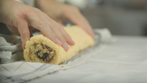 chef removes towel from a freshly baked and rolles swiss roll vegan desert with jelly jam in the middle