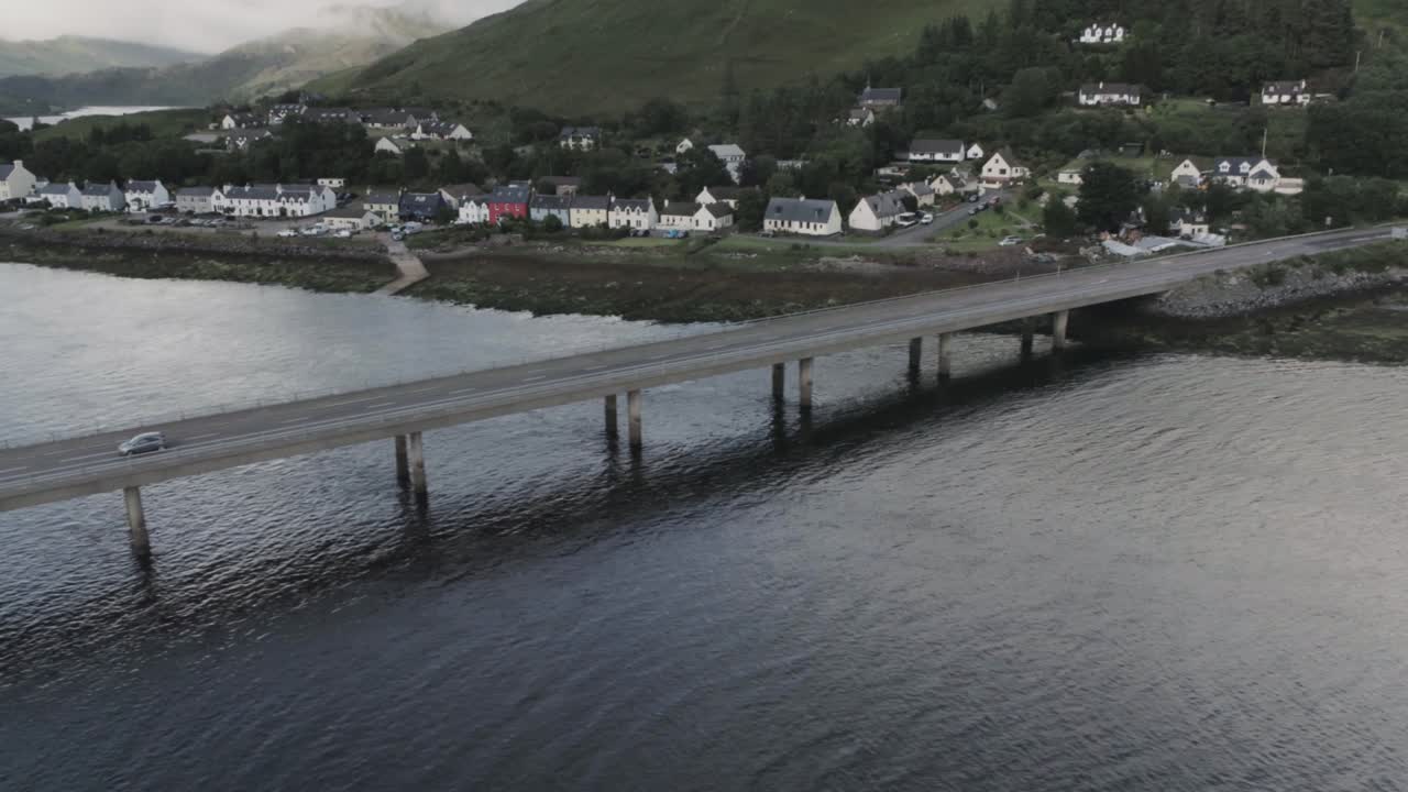 Panning drone shot tracking a car crossing the river Elchaig in Scotland showing the colourful village of Dornie in the background, scottish highlands