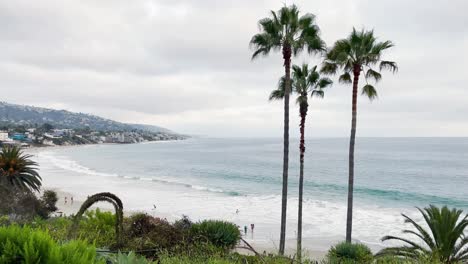 As-the-waves-roll-in-along-the-beach-of-the-California-shoreline,-people-walk-and-play-on-the-sand-and-in-the-surf