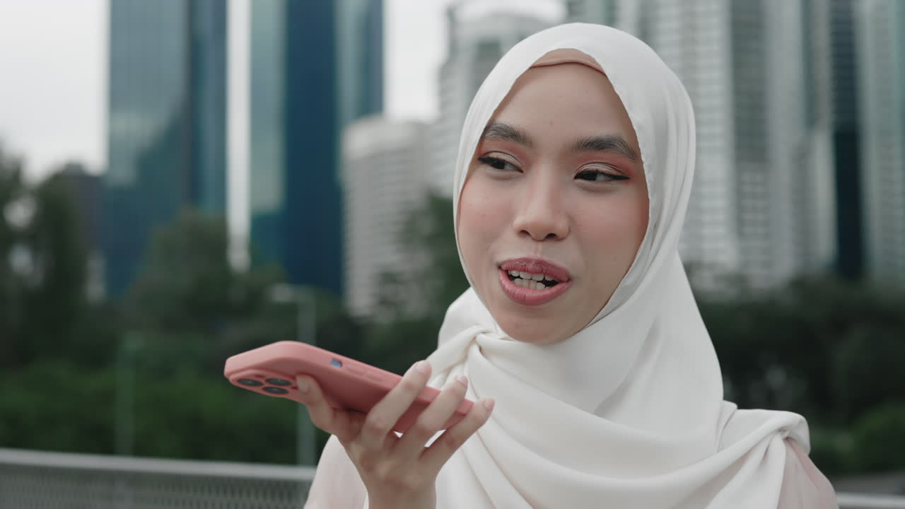 Woman in hijab using a smartphone for voice recording in a city