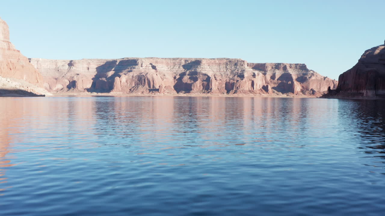 Racing over the water of Lake Powell, the camera slowly tilts up to reveal a stunning set of cliffs on the water's edge at sunset.