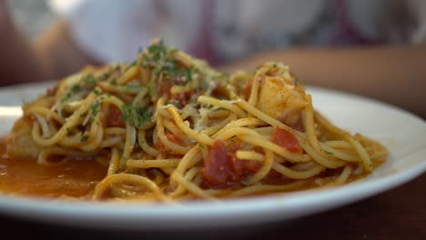 a little girl eats tomato seafood spaghetti in a restaurant. the subject is on the left.