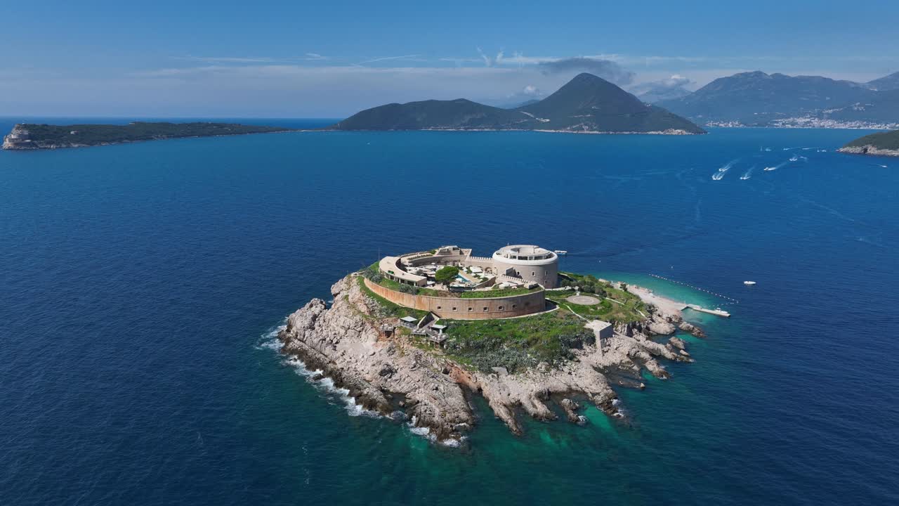 Aerial establishing view of Mamula Island, travel destination of Montenegro in Adriatic Sea, drone fly natural blue environment with mountain background