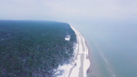 Hermosa-Vista-Aérea-De-La-Costa-Del-Mar-Báltico-En-Un-Día-De-Invierno-Nublado,-Playa-Con-Arena-Blanca-Cubierta-De-Nieve,-Erosión-Costera,-Cambios-Climáticos,-Disparos-De-Drones-De-Gran-Angular-Que-Avanzan