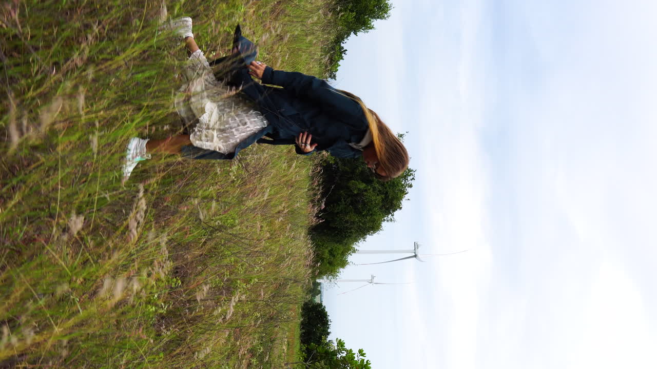 풍차 근처 필드에서 산책 드레스와 코트에 금발 소녀의 세로 돌리 오른쪽 샷