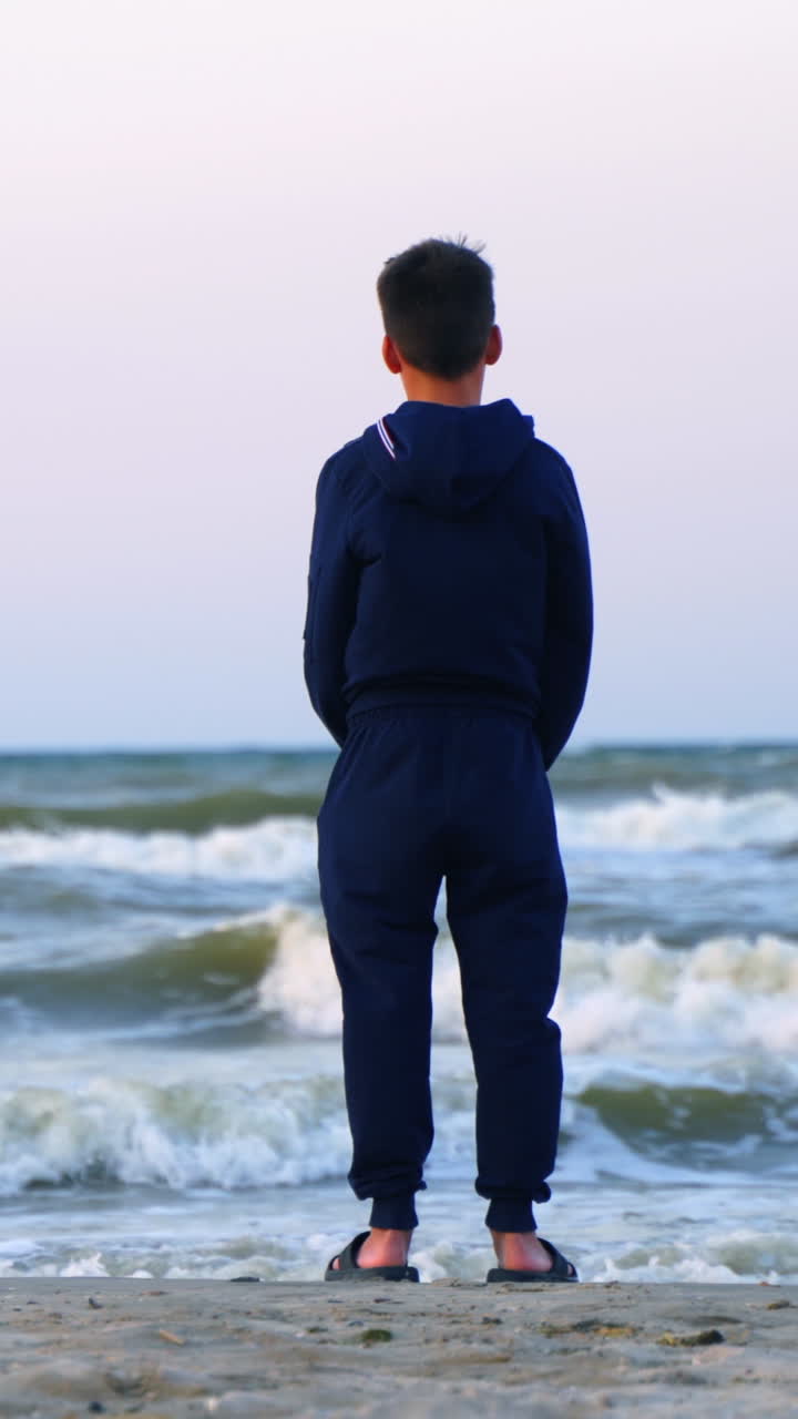 Boy standing on the beach. Rear view of standing boy near sea