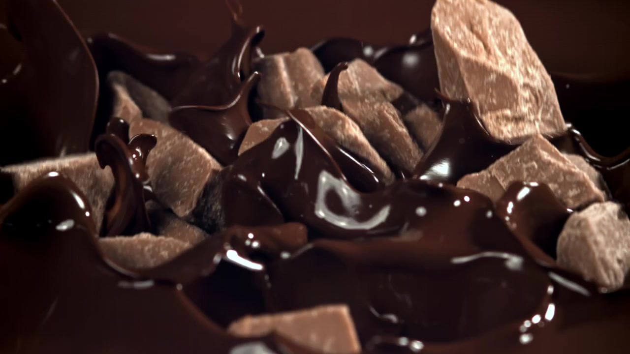 Slowmotion af chokoladestykker, der plasker ned i smeltet chokolade