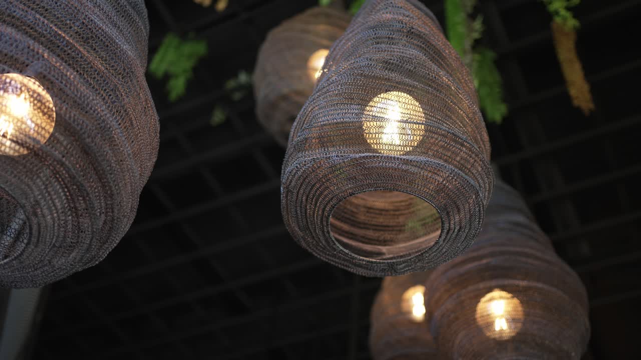 close up of glowing woven lampshades hanging from dark rustic ceiling