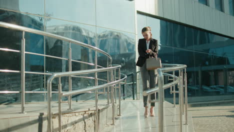 banker walking down office ramp after work, attentively checking handbag to retrieve car key, glass building reflecting urban environment, sunlight illuminating sleek metal railings