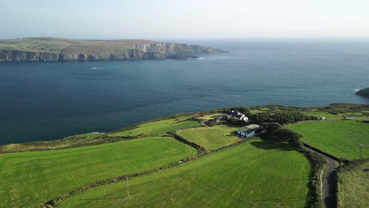 Farmland and road to the house with Atlantic ocean and distant cliffs of Mallavoge, an aerial at Mizen Head, West Cork Ireland