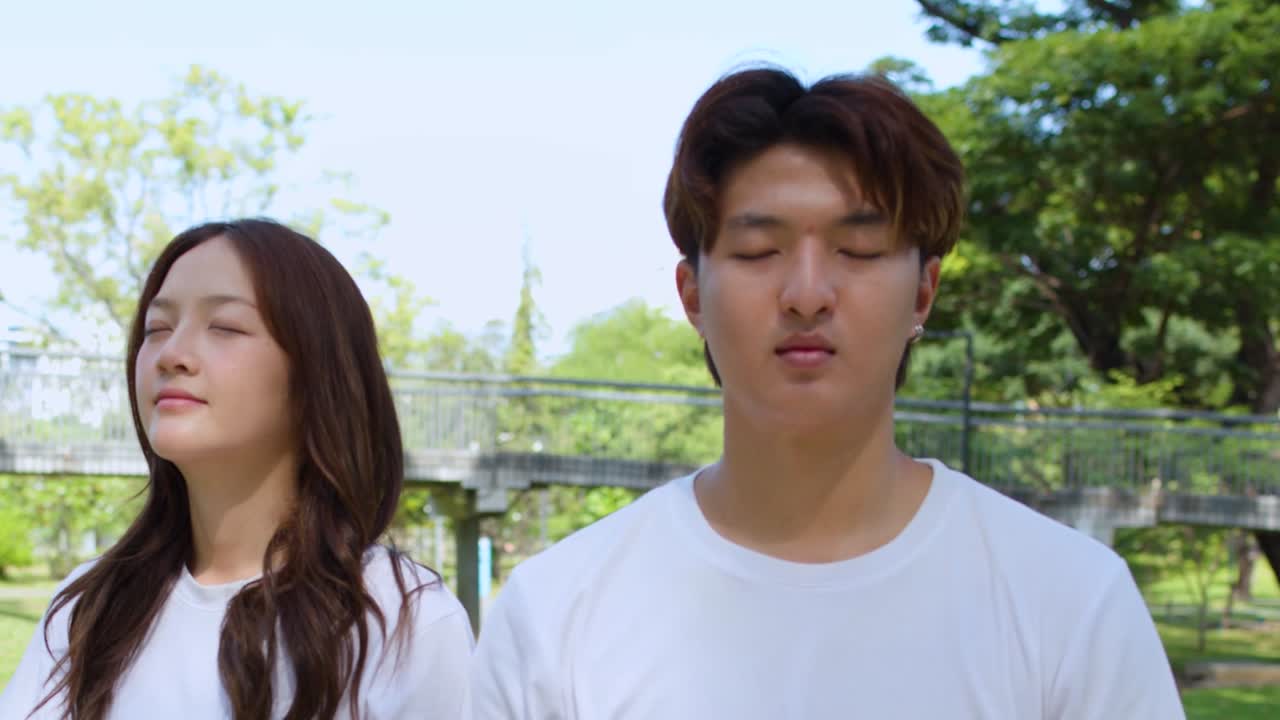 ชายหนุ่มและหญิงสาวในเสื้อเชิ้ตสีขาวฝึกเจริญสติโดยหลับตาอยู่ท่ามกลางธรรมชาติ