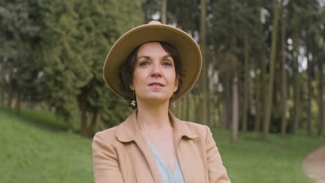 portrait of a middle aged woman in hat standing in the park and looking at the camera