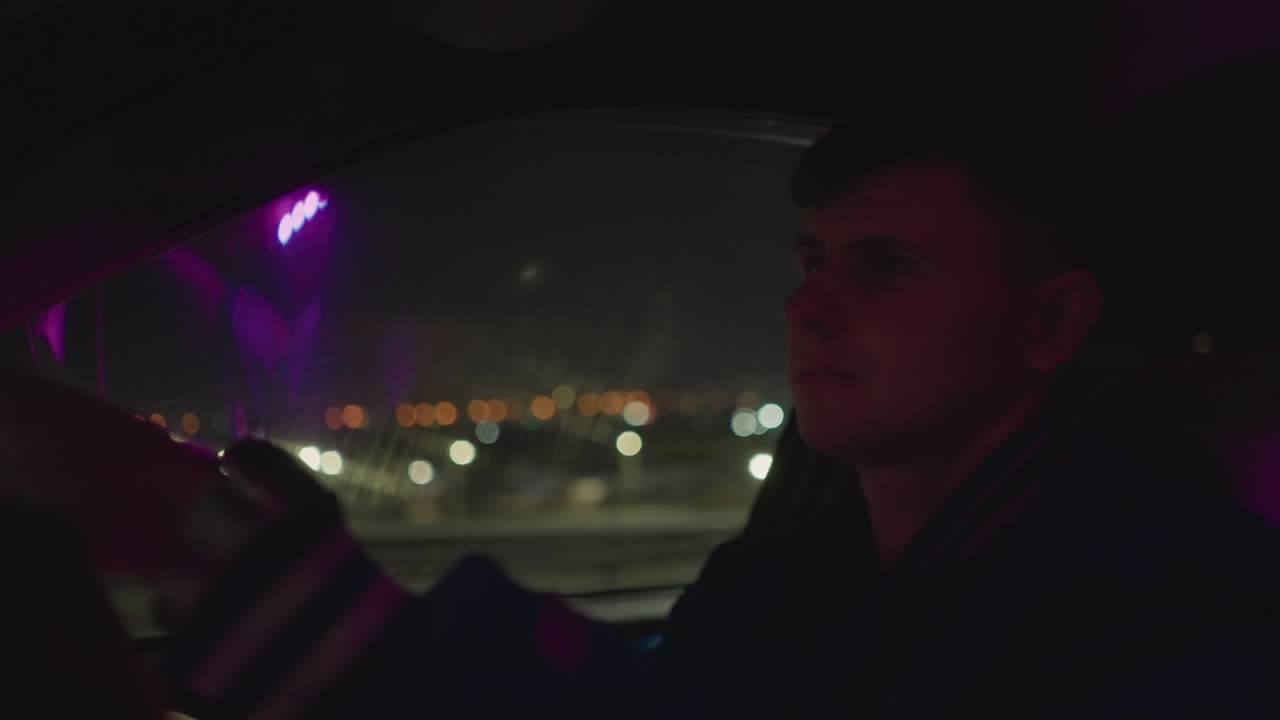 Mannlig sjåfør krysser opplyst bro om natten, bylys glitrer bak frontruten, stille langtransportpendler eller nattbud som ser fremover, lilla neonrefleksjoner på glass, sakte panorering