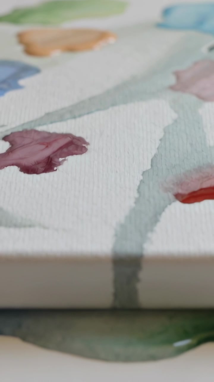 Video verticale: Raggiungendo il bordo, una velatura e tocchi color verde acqua su carta acquerello si diffondono in una pozzanghera sul tavolo.