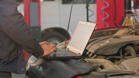 computer diagnostics of cars, young mechanic specialist male uses laptop technology while repairing vehicle with open hood at service station