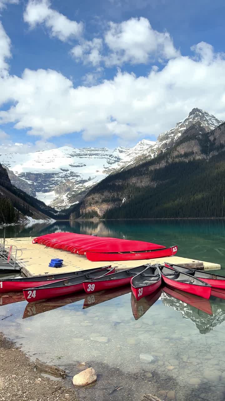 Canoe rosse ormeggiate su acqua turchese limpida che riflette montagne innevate e una foresta verde nel Lago Louise, Parco Nazionale di Banff.