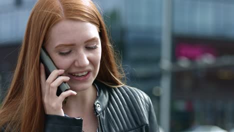 close up of young red-haired girl with freckles on the phone having a conversation in a big city wearing a black leather jacket