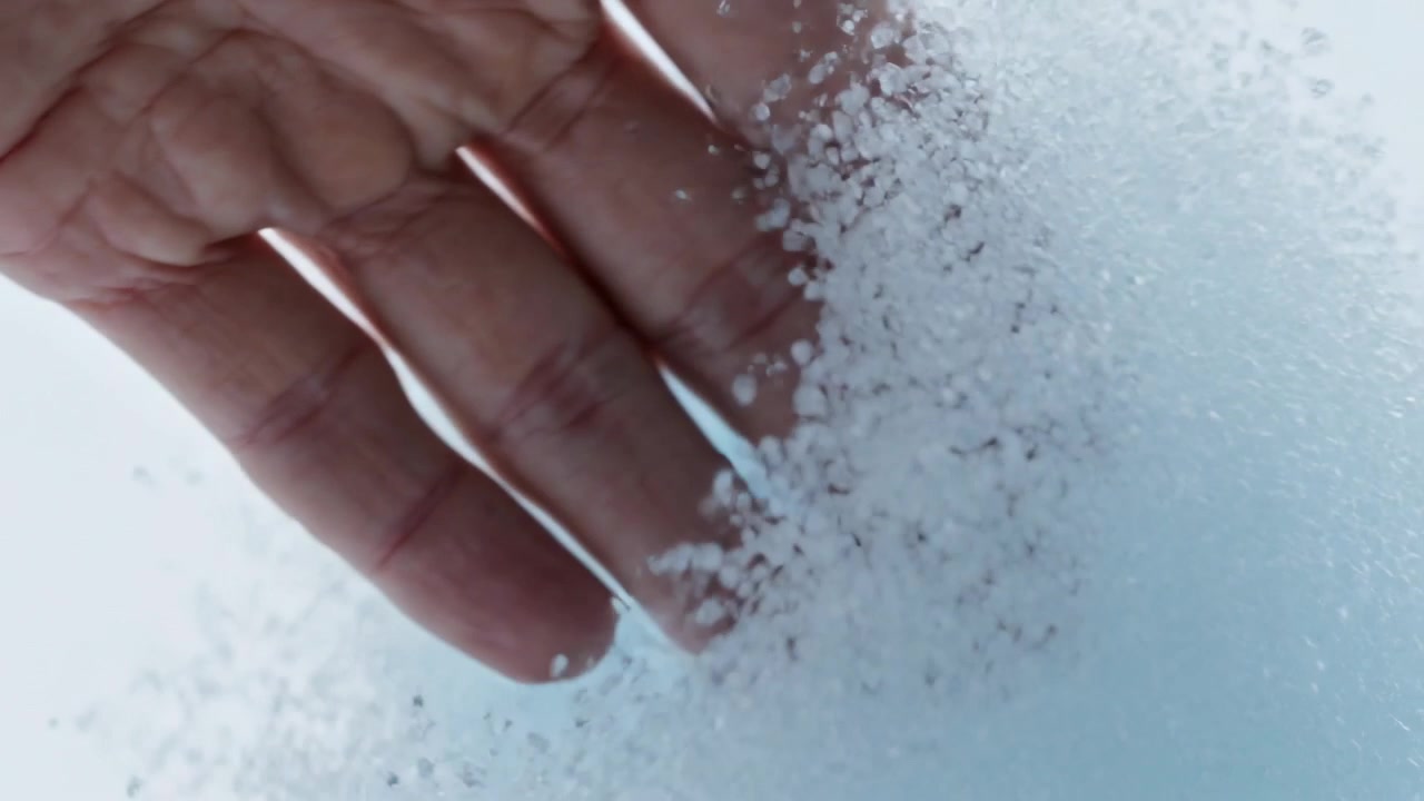 Mano che scivola da sinistra, preme attraverso un cumulo di schiuma in primo piano, rivelando un nucleo blu.