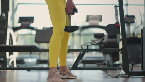 Young-Hispanic-brunette-woman-squats-holding-a-dumbbell-in-the-gym-in-a-yellow-tracksuit