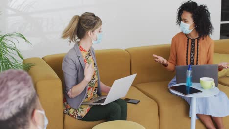 dos mujeres con máscaras faciales hablando entre sí en la oficina