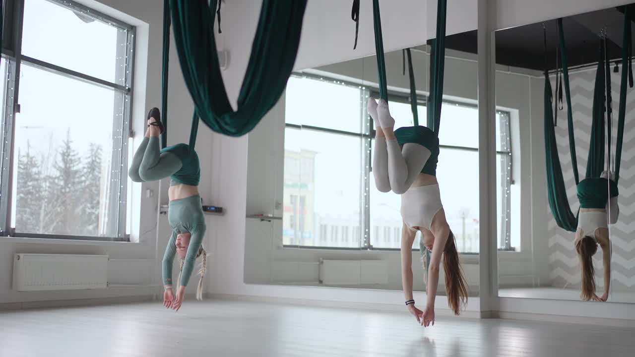 The interior shooting of an two women practices different inversion antigravity yoga with a hammock in yoga studio. The balance between mental and physical two person effort and achievement concept