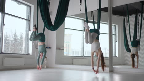 the interior shooting of an two women practices different inversion antigravity yoga with a hammock in yoga studio. the balance between mental and physical two person effort and achievement concept