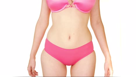 with an uncomfortable expression, a woman wearing a pink bra and underwear, trying to hide her tummy with her two hands