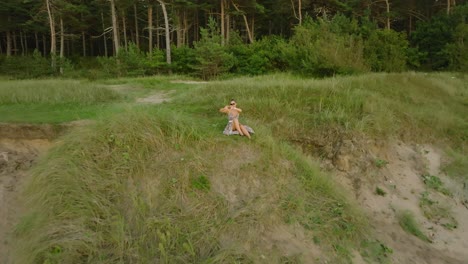 vista aérea de una hermosa joven caucásica romántica con un vestido largo en la playa de arena blanca, signo de amor con las manos, noche soleada de verano, puesta de sol, amplia toma de drone ascendente moviéndose hacia atrás
