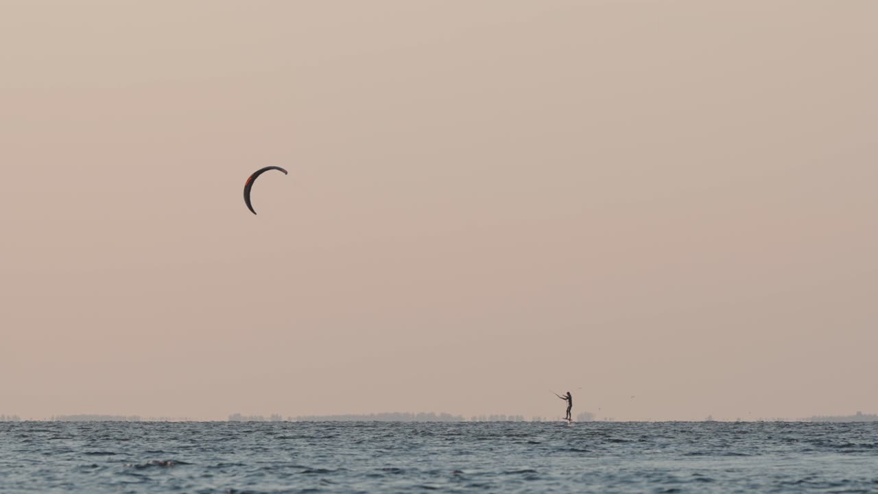 un kitesurfista solitario navegando en vientos ligeros, con la luz dorada del atardecer