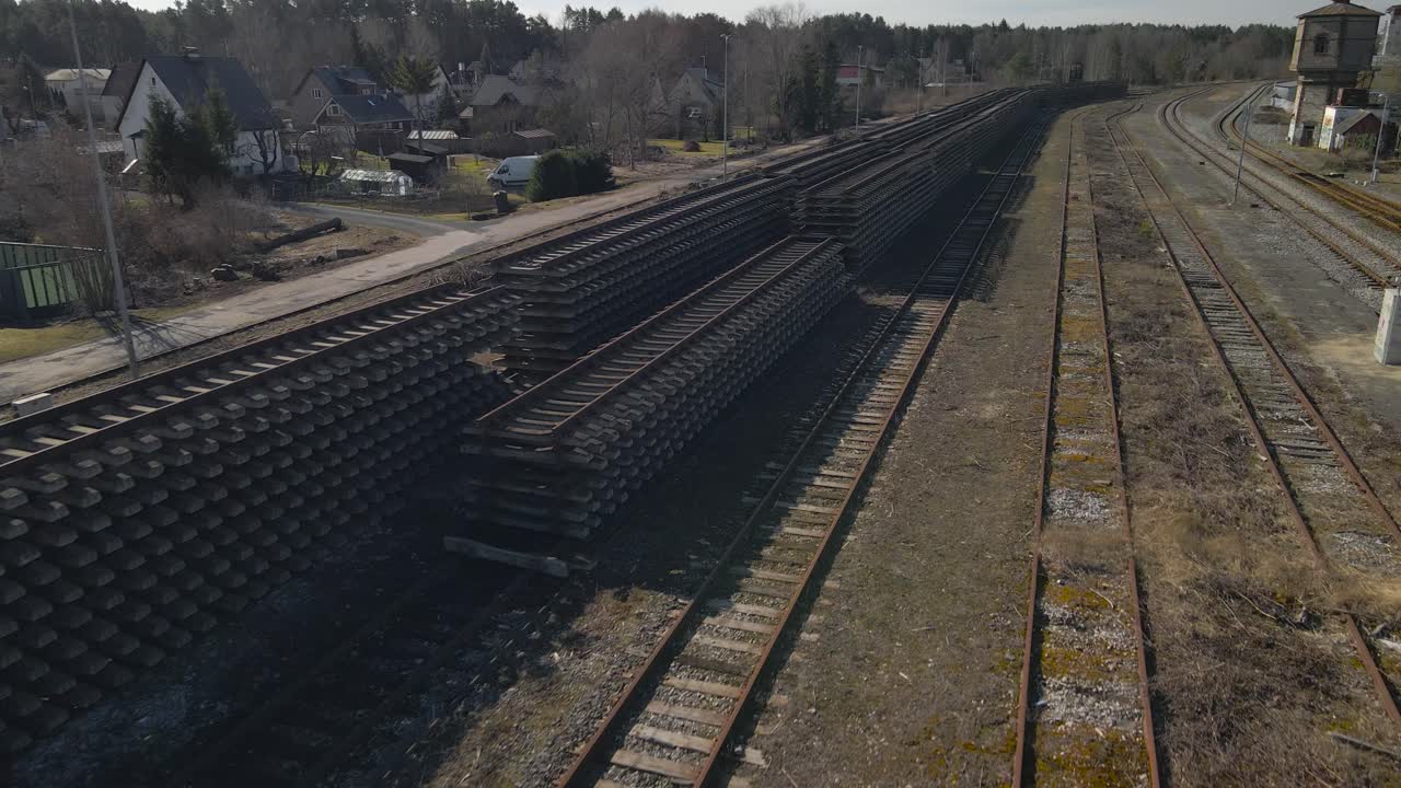 Aerial drone footage gliding over rusty brown metallic old vintage railroad or traintracks in Tallinn city during a sunny spring day while granite gravel is visible between the tracks and brown grass