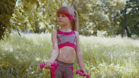 Athletic-young-sporty-fit-child-kid-girl-doing-dumbbells-workout-in-park-performing-bicep-exercising