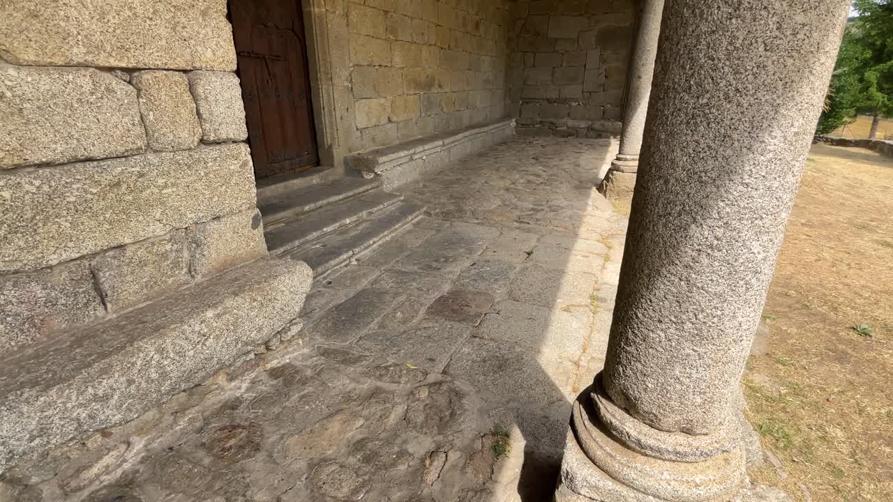 Slow motion filming of a entrance porch with granite columns, the floor is made of stone and we see magnificent wooden ceilings in wood accompanied by an iron and wood door in the same style.