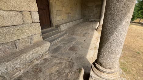 slow motion filming of a entrance porch with granite columns, the floor is made of stone and we see magnificent wooden ceilings in wood accompanied by an iron and wood door in the same style.
