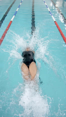 vertical video: swimming in pool, athlete performing backstroke in competition lane with focus
