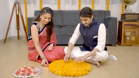 Indian-couple-decorating-home-with-Rangoli-and-Earthen-lamps