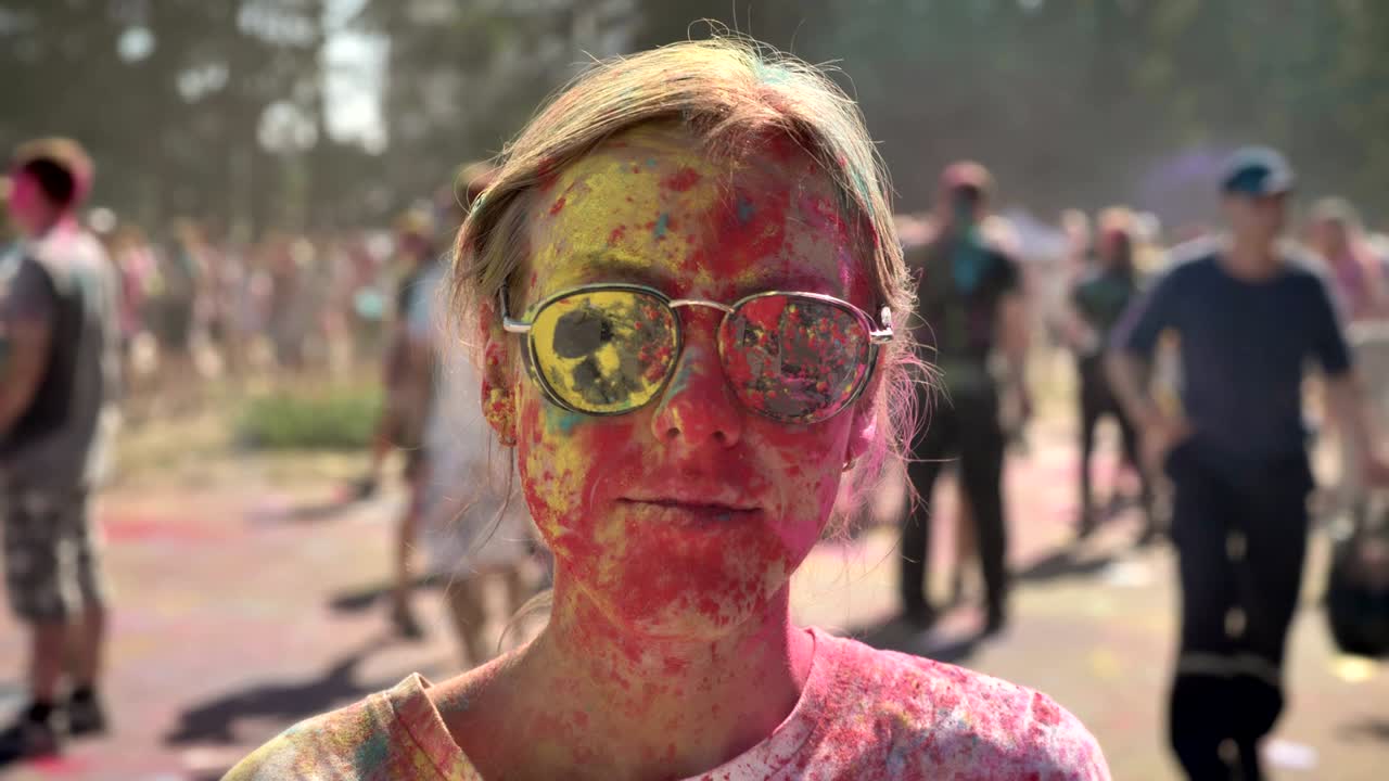 Young pretty girl in colors with sunglasses is thrown with colourful powder on holi festival in daytime in summer, laughing, color concept