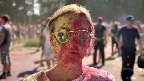 young pretty girl in colors with sunglasses is thrown with colourful powder on holi festival in daytime in summer, laughing, color concept