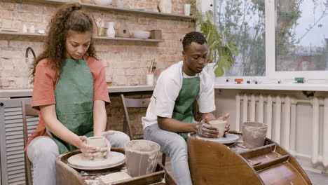 empleados que usan delantal verde modelando piezas de cerámica en una rueda de alfarero en un taller