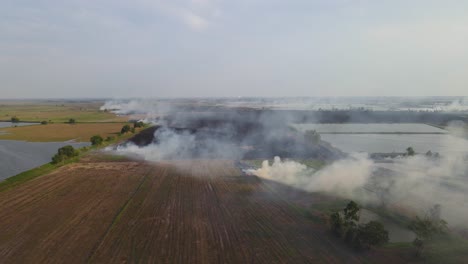 reverse aerial footage of this tilled farmlands burning as the farmers prepare for the planting season, pak pli, nakhon nayok, thailand