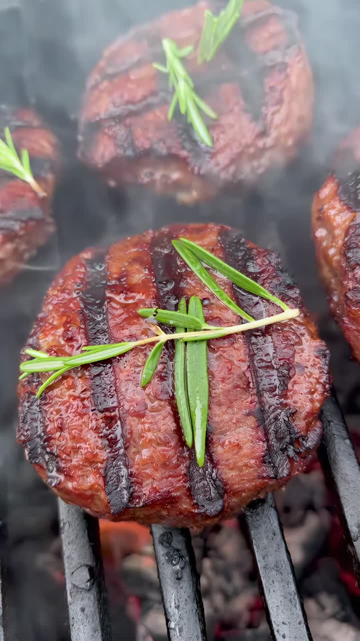Close-up video of sizzling grilled burgers with rosemary, capturing smoky textures and flavors