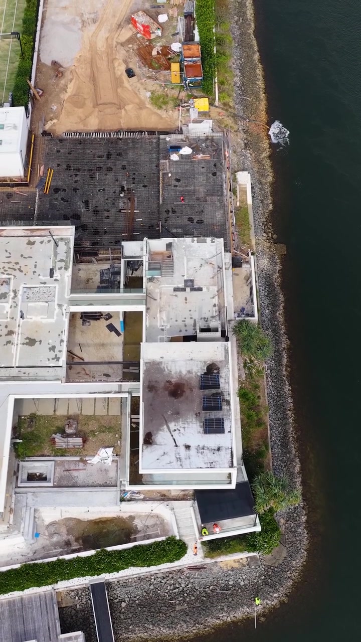 Top-down drone shot reveals modern mansion architecture and adjacent residential construction on a canal.