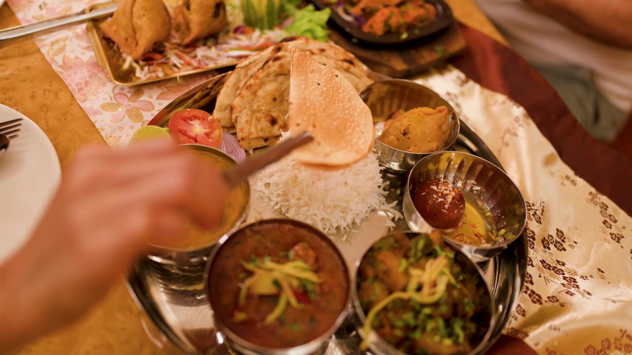 Overhead view of person eating diverse Indian dishes from a metal thali plate indoors.