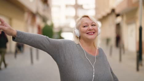 middle age blonde woman listening to music using smartphone and dancing at street