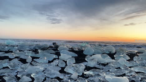 Toma-Panorámica-Fija-A-Nivel-Del-Suelo-De-La-Puesta-De-Sol-Con-Hielo-Glacial-En-El-Primer-Plano-De-La-Playa-De-Diamantes-En-El-Sur-De-Islandia