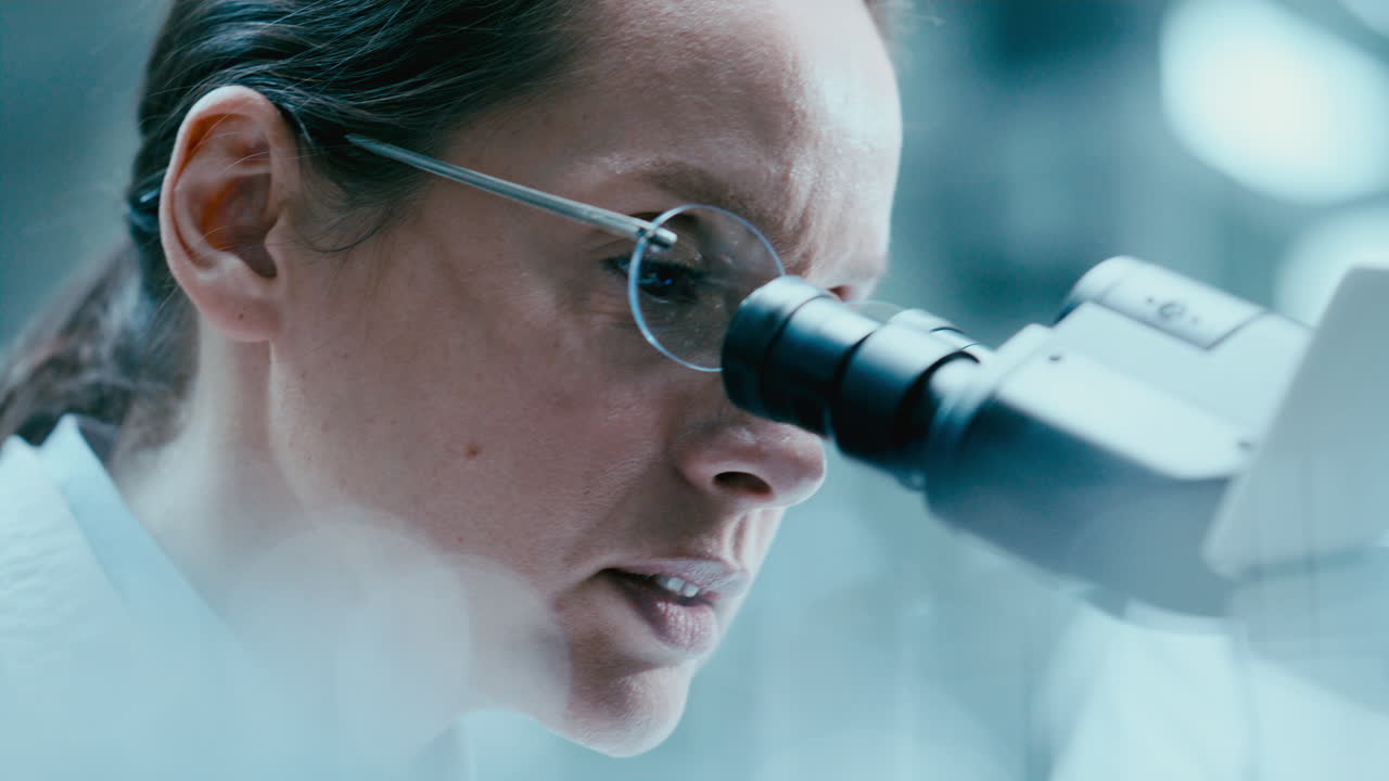Assistente di laboratorio che prende appunti mentre una scienziata lavora al microscopio